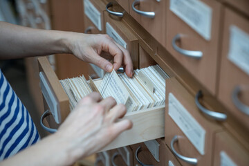 Woman finding book cars in university cards index catalog in library. Student goes through cards and looks for right one. Education in college, school, searching literature for study, learn concept.
