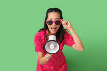 Young Asian woman with megaphone on green background