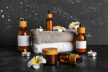Composition with different cosmetic products, clean towels and burning candles on dark background