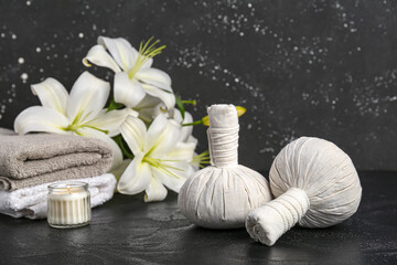 Massage herbal bags, clean towels and beautiful lily flowers on dark background