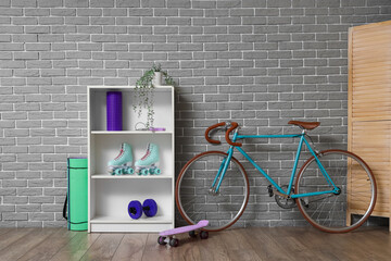 Shelf unit with sports equipment and bicycle near grey brick wall in room