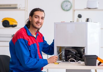 Young male contractor repairing refrigerator at workshop