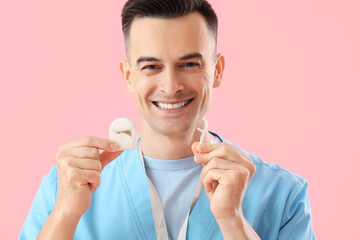 Male dentist with floss and toothpick on pink background, closeup
