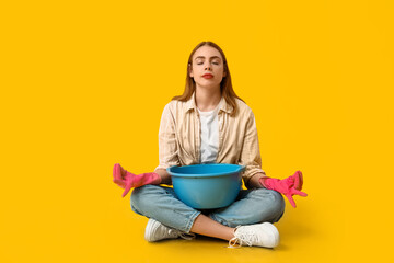 Beautiful young housewife with basin meditating on yellow background. Zen concept