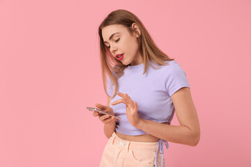 Fototapeta premium Young beautiful woman with mobile phone on pink background