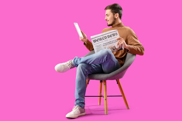 Young man with newspaper and tablet computer in armchair on purple background - obrazy, fototapety, plakaty