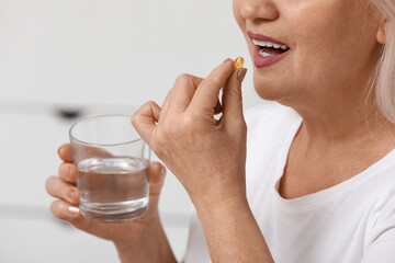 Fototapeta premium Beautiful mature woman with glass of water taking pill at home
