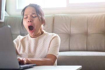Asian women Sitting and yawning while working with laptop in morning