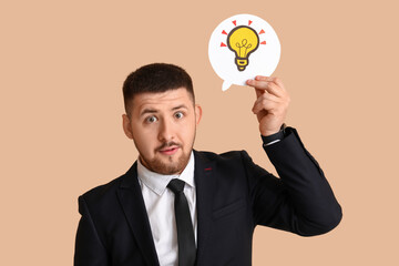 Young businessman holding speech bubble with drawn light bulb on beige background. Business idea concept