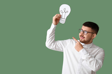 Young businessman pointing at drawn light bulb on green background. Business idea concept