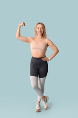 Beautiful young sporty woman showing muscles on blue background. Weight loss concept