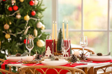 Christmas table setting with burning candles and fir cones in room