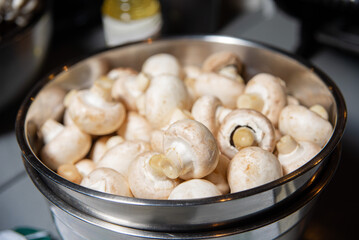 A Bowl of Fresh Mushrooms Waiting to be Cooked. A metal bowl filled with mushrooms on top of a kitchen table.