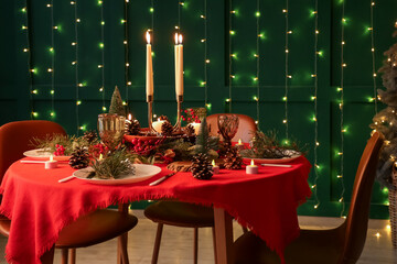 Festive dining table set for Christmas with burning candles and fir cones in room