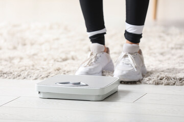 Beautiful young Asian woman with scales in living room at home, closeup. Weight loss concept