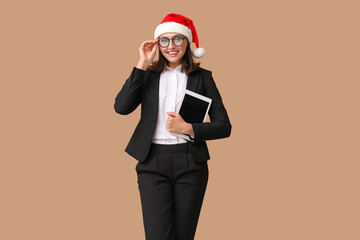 Beautiful businesswoman in Santa hat with tablet on brown background