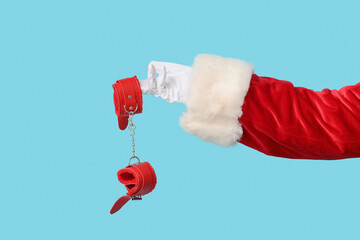 Santa hand with handcuffs from sex shop on color background, closeup