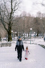 Fototapeta na wymiar Mom and little girl are walking in a snowy park holding hands