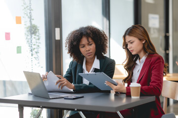 Two business woman using laptop talking and consulting working together in the office. Two business colleagues having a discussion during a meeting.