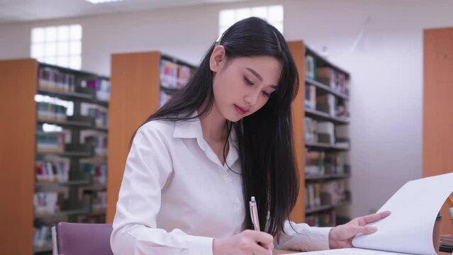 Young Asian female university students are actively reading books to study, research, and summarize lessons, preparing for exams in the university library. dedicated approach to academic exploration