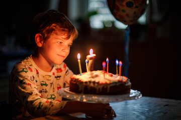 Adorable happy blond little kid boy celebrating his birthday. Child blowing seven candles on...