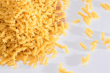 Uncooked Fusilli Pasta Scattered on Wooden Board and White Table. Raw and Dry Macaroni. Fat and Unhealthy Food