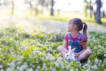 Fototapeta premium a little girl with a rabbit in a meadow with a clover are looking into the distance 
