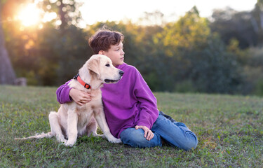 a boy and a golden retriever are sitting together in a meadow at sunset and looking in the same direction