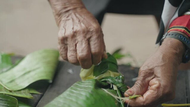 Closeup of Hands making a knot into Banana leaves, sealing them to put it over fire, Peru