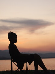 Silhouette of a young man sitting by the lake enjoying the sunset. peaceful atmosphere in nature
