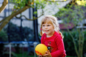 Little adorable toddler girl playing with ball outdoors. Happy smiling child catching and throwing, laughing and making sports. Active leisure with children and kids.