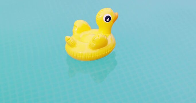 Inflatable yellow duck swims in swimming pool of clear blue water on sunny day