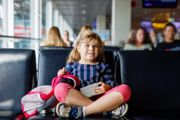 Little girl at the airport waiting for boarding at the big window. Cute kid holding passport..Looking forward to leaving for a family summer vacation