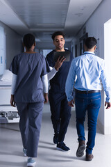 Biracial male doctor using tablet walking in hospital corridor