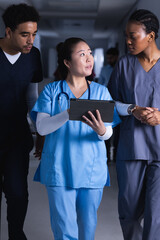 Diverse male and female doctors talking and using tablet walking in hospital corridor