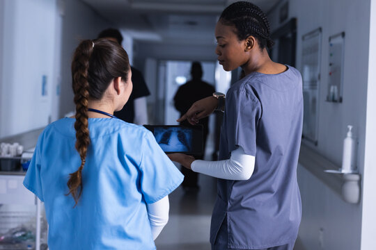 Diverse female doctors talking and using tablet in hospital corridor