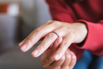 Closeup image of a woman putting on a silver ring on her ring finger