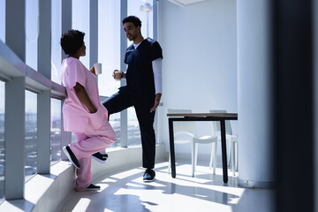 Diverse male and female doctors talking and drinking coffee in sunny hospital