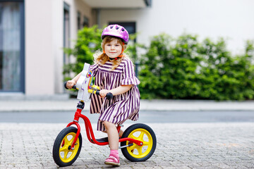 Little toddler girl running with balance bike on summer day. Happy child driving, biking with bicycle, outdoor activity. Happiness, childhood
