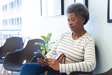 African american senior woman using smartphone in hospital waiting room