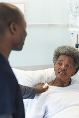 African american male doctor talking with senior female patient in sunny hospital room