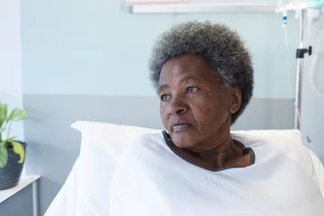 Fotobehang African american senior female patient lying in bed in sunny hospital room © wavebreak3