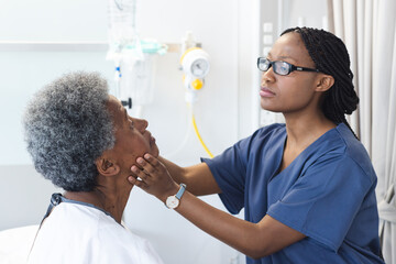 African american female doctor testing eyes of senior female patient in hospital room