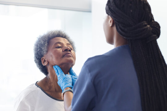 African american female doctor testing neck of senior female patient in hospital room