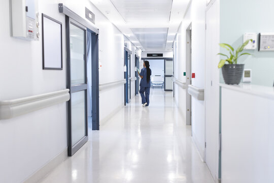 Back Of African American Female Doctor With Documents Walking In Hospital Corridor