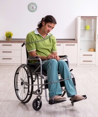 Young male invalid in wheel-chair suffering at home