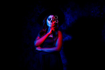 Fototapeta na wymiar A women with Halloween Makeup in blue red light giving out a horror look wearing black gown in black background