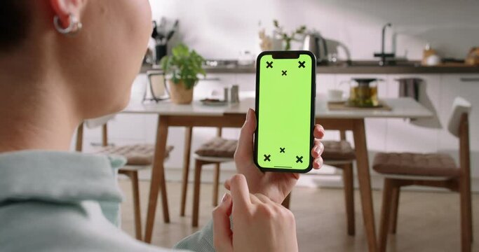 Smartphone held in woman's left hand displays green screen with tracking points. Scrolling feed and tap at bottom, online shopping. Placing order in online store, adding items to cart. App advertising