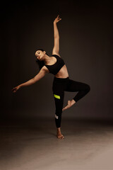 Slim girl performing yoga arts wearing black sports dress in black background performing yoga poses...