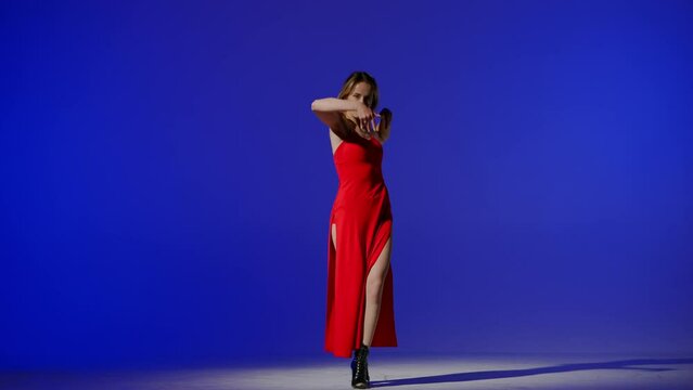 On a blue background. Young woman, showing dance moves towards high heels. A spotlight beam shines on her and gives her a shadow, the edges of the background are darkened. She is rhythmic, plastic